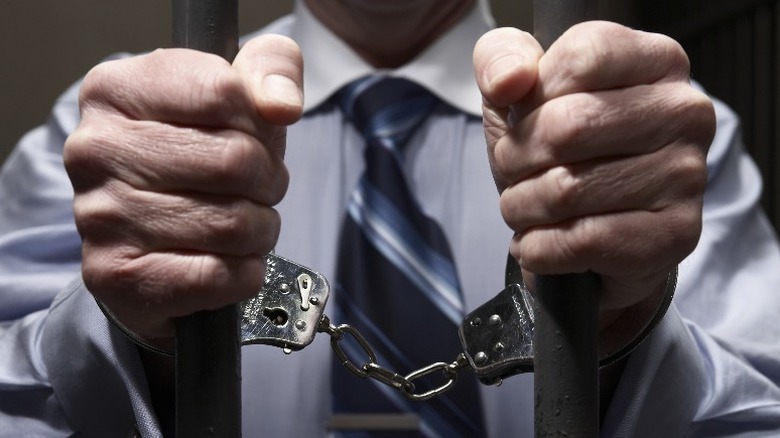 handcuffed man's hands on prison bars