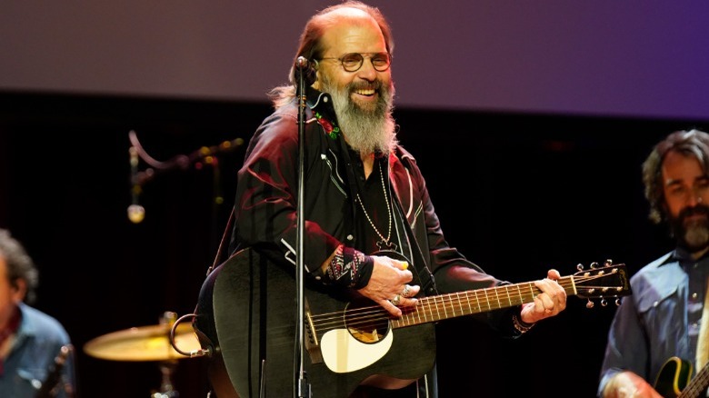 Steve Earle onstage, smiling, playing guitar