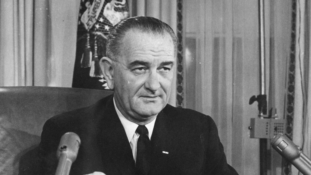 Lyndon B. Johnson sitting in front of microphones