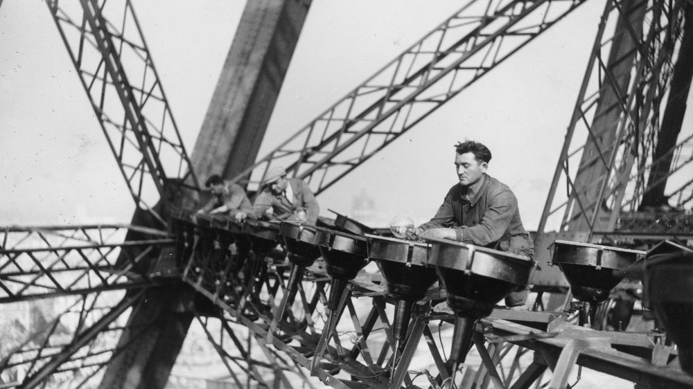 29th October 1937: Electrical workers balance high up on the Eiffel tower in paris to change the lights that illuminate the tower at night.