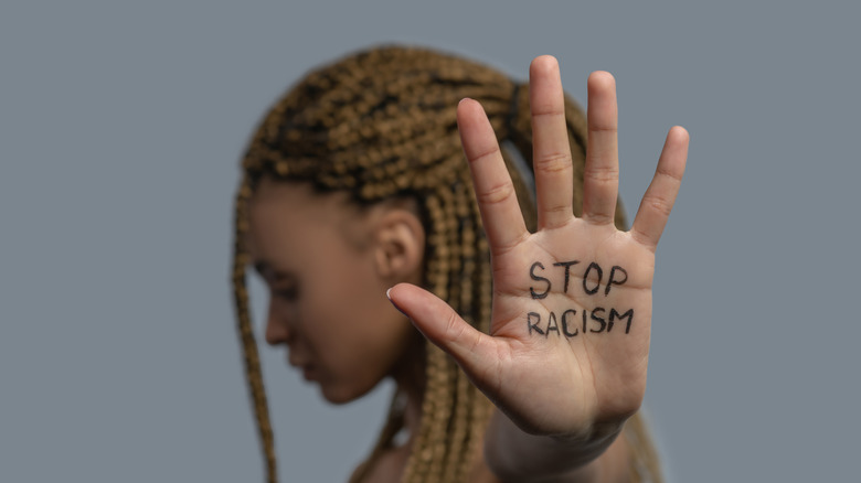 A Black woman looking away, holding up her hand, on which is writing "Stop racism." 