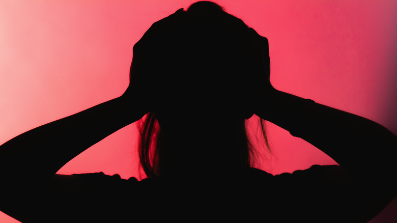 Silhouette woman clutching head, red background