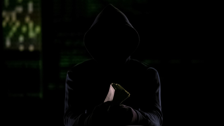Man in dark hoodie holding money