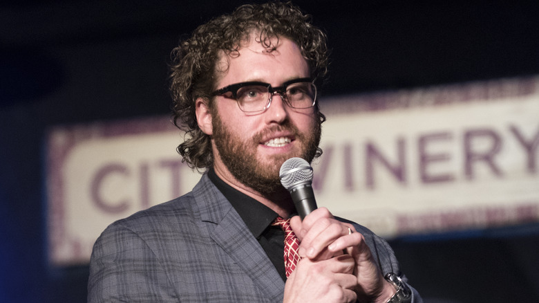 T.J. Miller glasses suit holding microphone