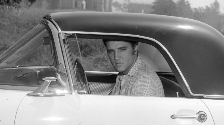 Elvis Presley sits behind the wheel of a car