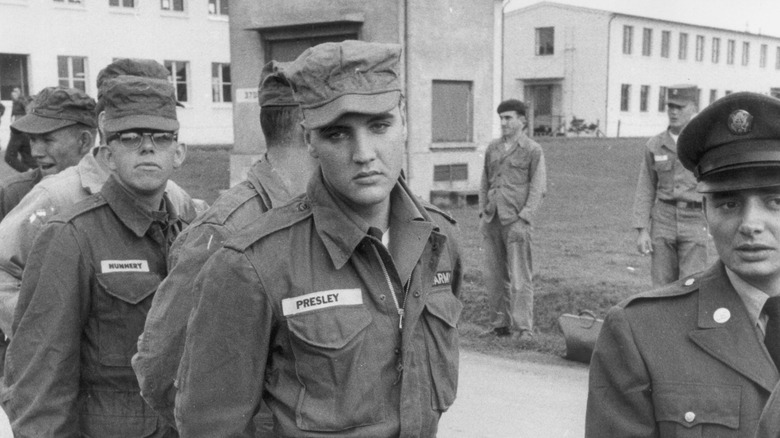 Elvis Presley frowns while standing in line with enlisted men