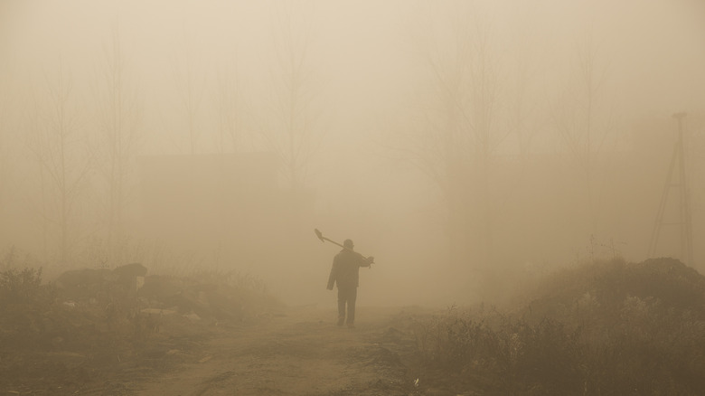 Person carries shovel through smog
