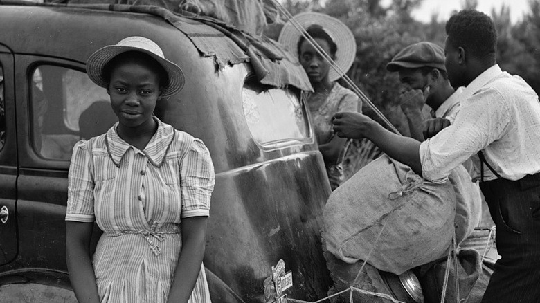 Black girl posing in front of her family as they pack their car, circa 1940