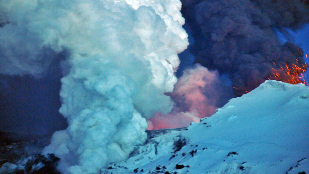 aerial view of volcano erupting over snowy mountain