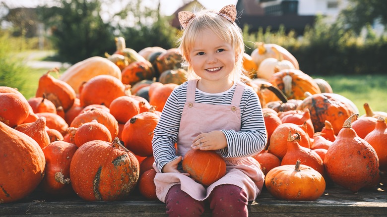 Child sitting at outdoor table of pumpkins