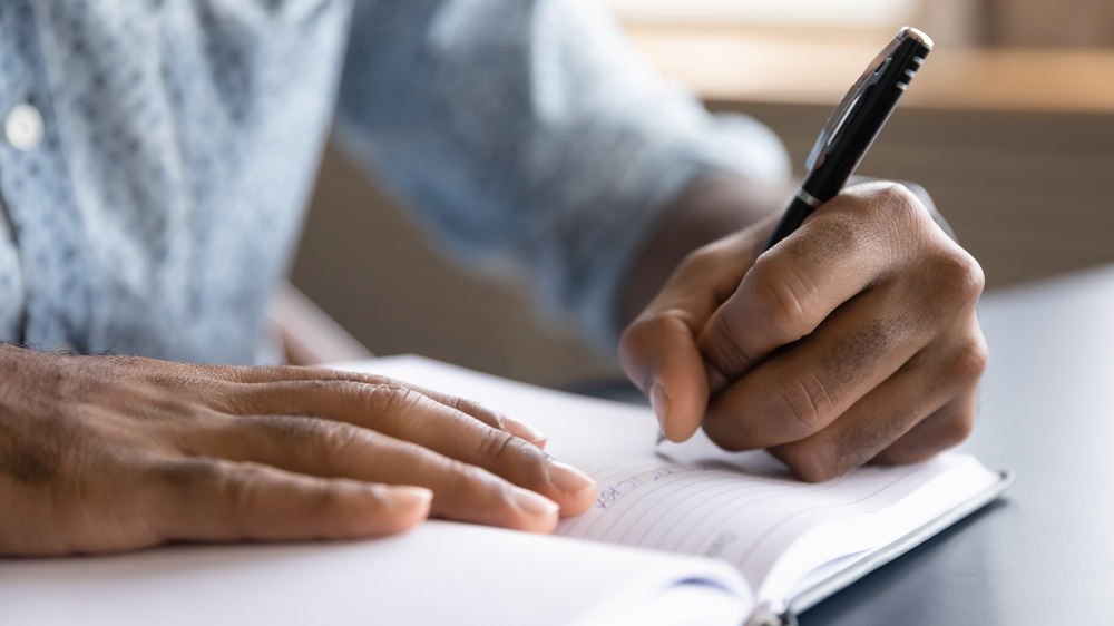 Close up view of Black left-handed businessman writing in notebook