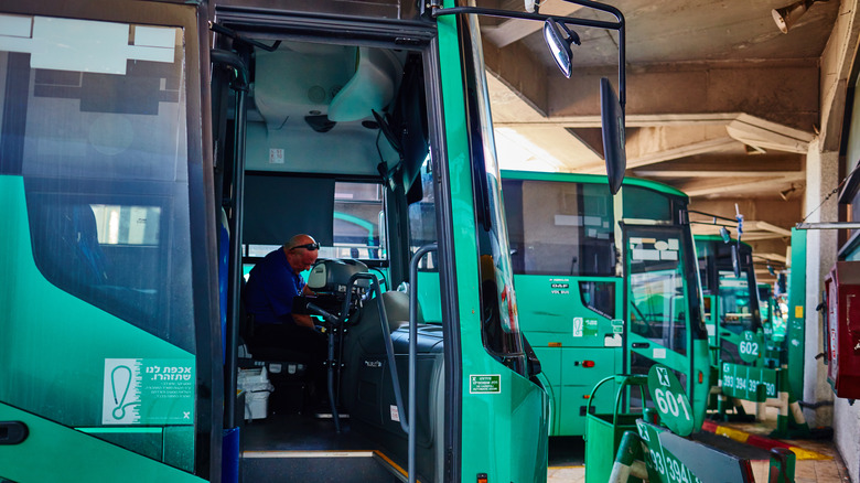 Door of the green Egged bus open to drivers seat with bald man with sunglasses on his head sitting in the drivers seat