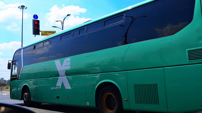 Side of green Egged bus with X logo plainly visible, stopped at a red stop light