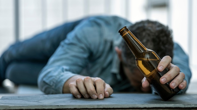 A man lying face down on cement with a bottle in his hand