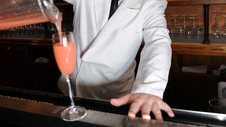 Hands pouring a Bellini cocktail into a glass