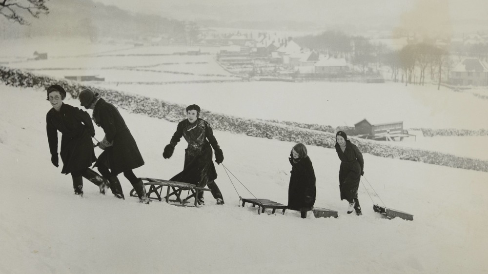 Young people walk up a hill with their sleds in Derbyshire in the 1900s.