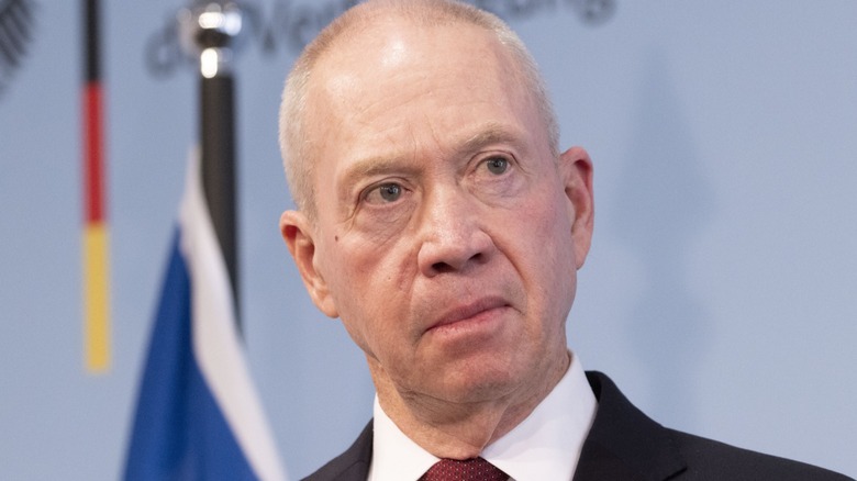 Yoav Gallant angry and serious in front of a flag