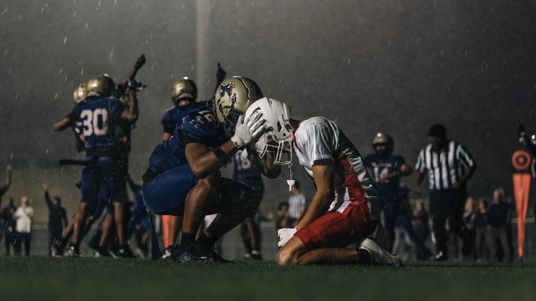 Two football players touching their helmets together while kneeling