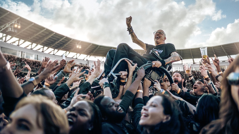 A crowd holding a man in a wheelchair over their heads.