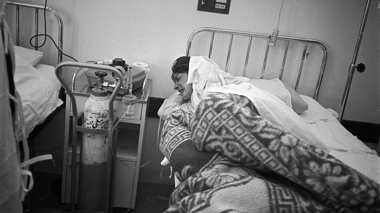 Black and white image of a Kurdish woman in the hospital with severe chemical burns on her face, wearing white robe 