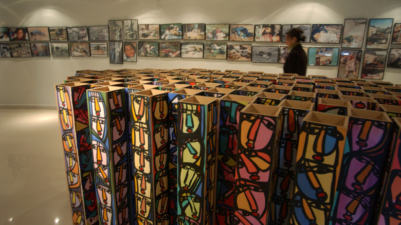 Kurdish woman walks past multicolored sculpture representing 5,000 faces and photos of victims of the March 16, 1988 chemical attacks on Halabja at a museum and memorial. photographs of the Halabja massacre line up the background behind the woman walking