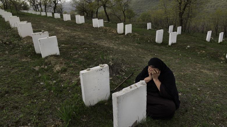 Kurdish woman sitting cross-legged and weeping with her head in her hands next to a white grave among a row of numerous white graves, all for Kurdish people who were killed during the Anfal campaign