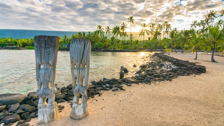 Carved hawaiian monuments on beach palm trees