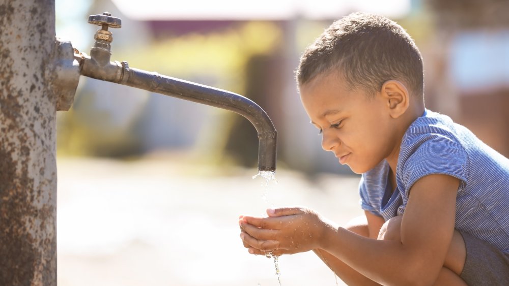 African child drinking water from tap outdoors.