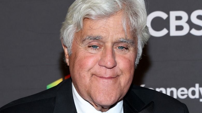 Jay Leno wearing black suit and smiling sadly