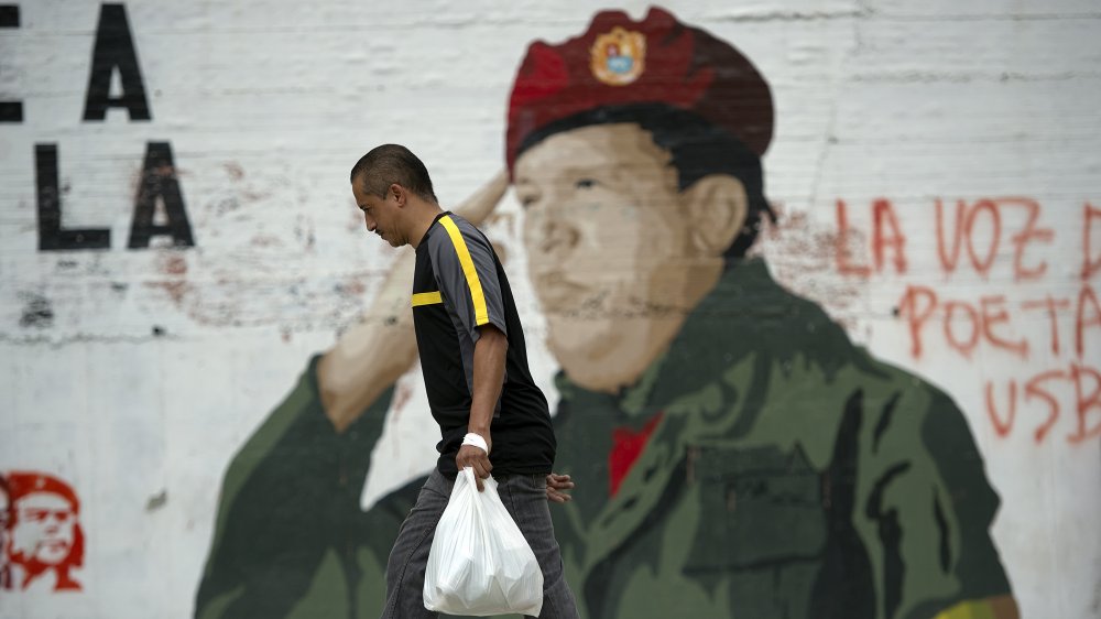 A man walks in front of a Hugo Chavez mural