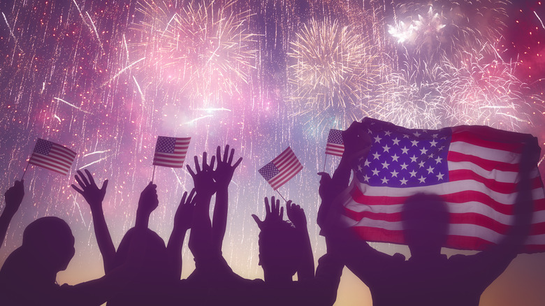 People holding U.S. flag in front of fireworks