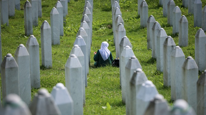 Muslim woman kneeling between Srebenica gravestones