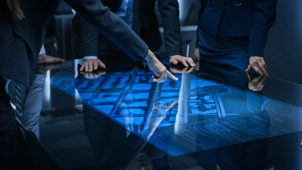 Ominous suited figures standing around and pointing at a digital display