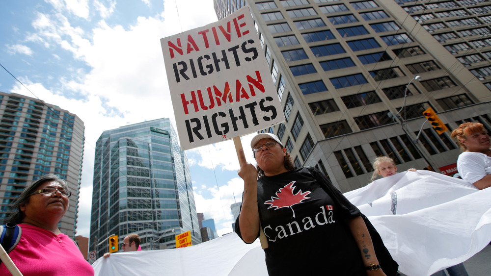 First Nationas woman hold a sign reading "Native Rights Human Rights"