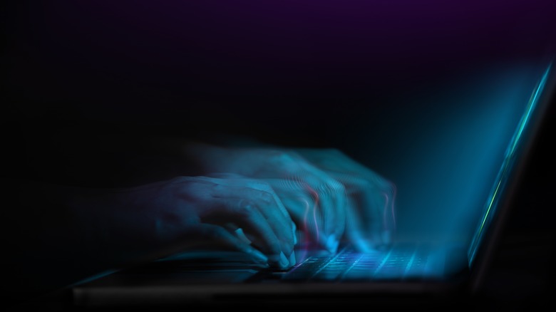 Blue lit hands typing on laptop black background