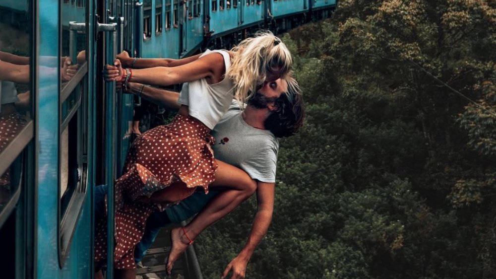 dangerous social media photo, woman kissing man while hanging outside a blue train over jungle ravine