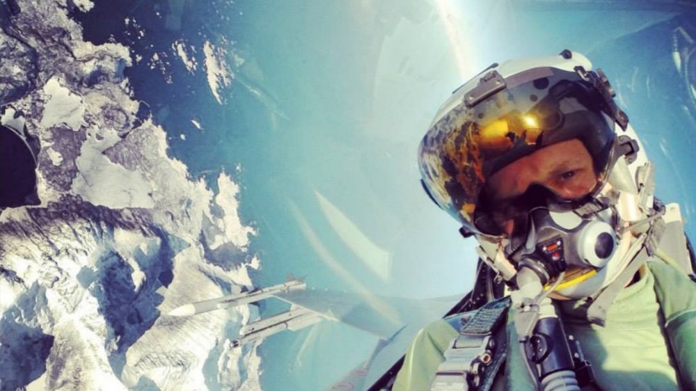 dangerous social media photo, male fighter pilot in full gear in a plane flying away from land and above two missiles