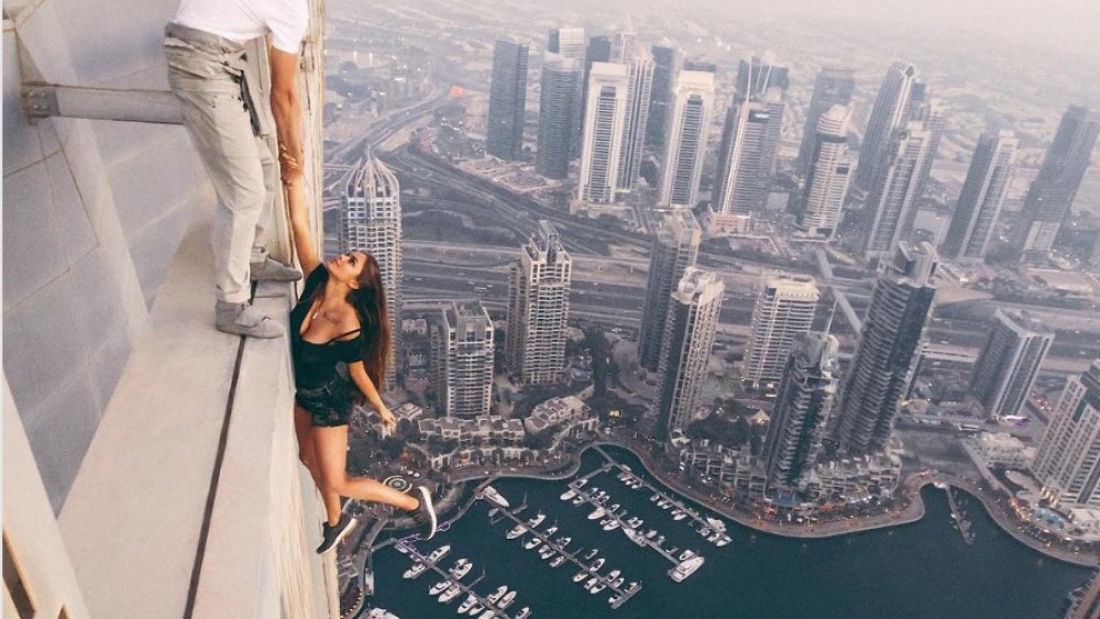 dangerous social media photo, man holding dangling woman off the side of a skyscraper