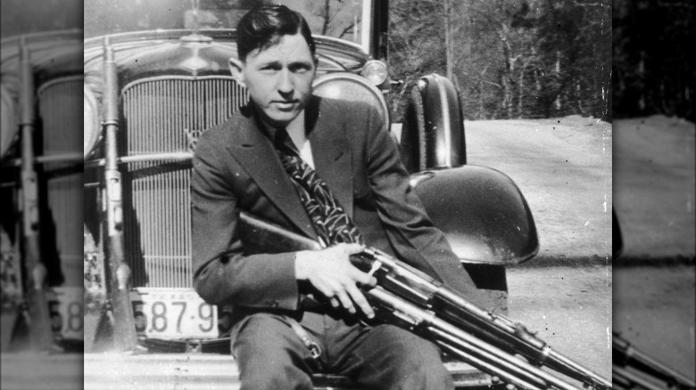 Clyde Barrow holding two rifles by car