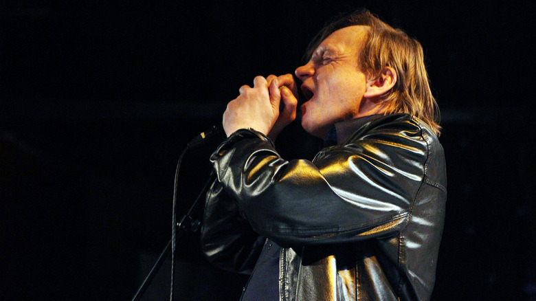 Mark E Smith in leather jacket with mic