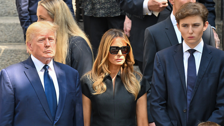 Donald, Melania, and Barron Trump looking sad after a funeral