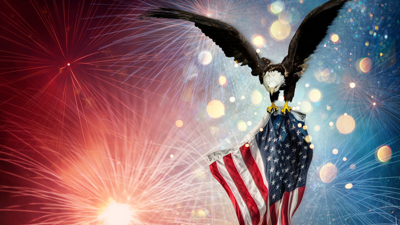 Bald eagle gripping American flag amidst fireworks