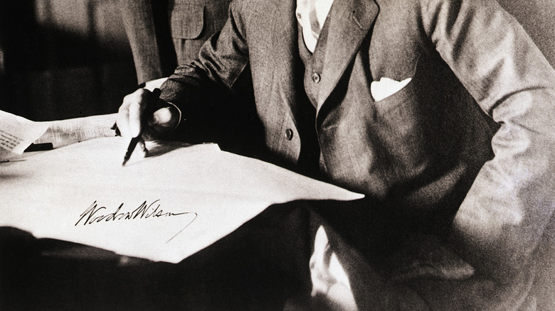 Woodrow Wilson looking over a document with pen in hand.