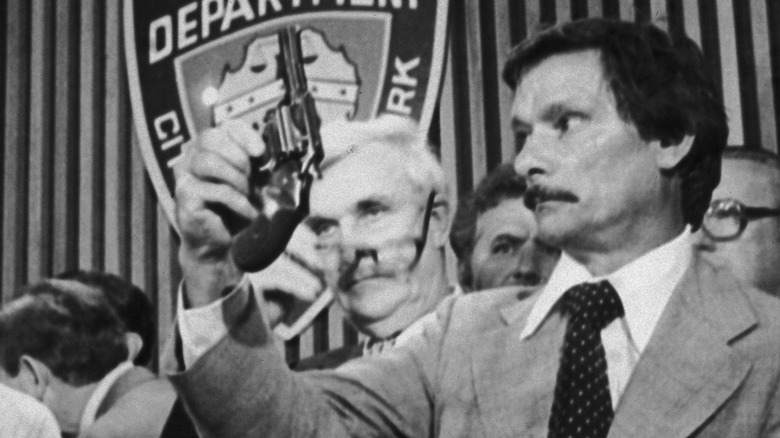 Edward Zigo holding up a revolver as New York mayor looks on