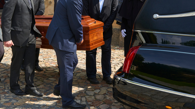 Funeral goers placing casket in hearse