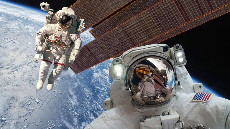 Two astronauts floating above planet and space station