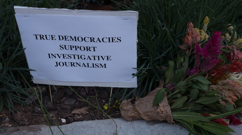Flowers and a sign reading "true democracies support investigative journalism"