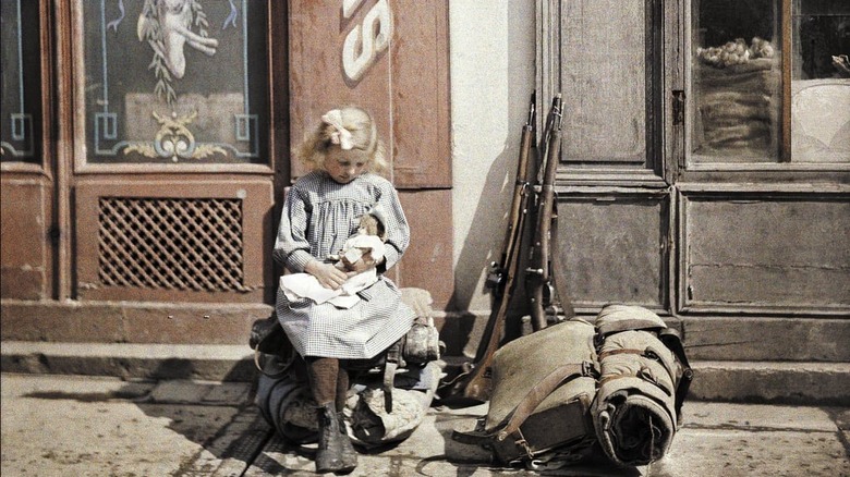 Girl with doll sat by rifles