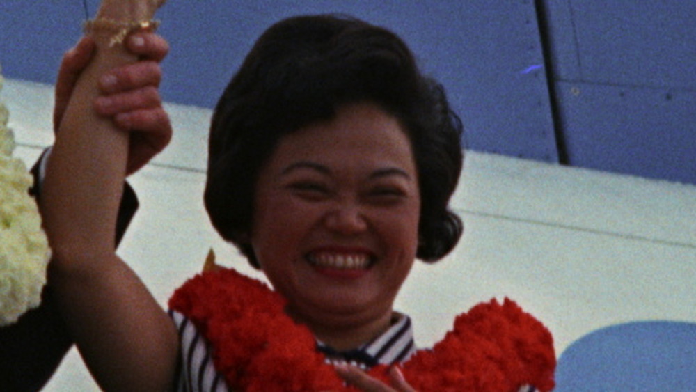 Patsy Mink standing at the entrance of Panam aircraft wearing a lei and waving