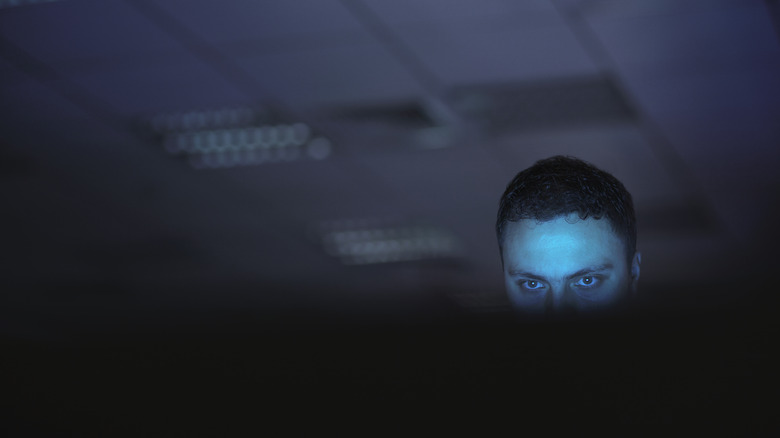 A man seated at the screen in a dark office